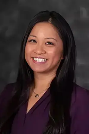 woman with black hair and purple shirt smiling at camera
