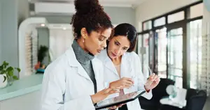 Two doctors in white lab coats examining a tablet in a medical office.