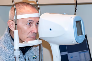 A man is looking into an optical machine with a white headband on his forehead.