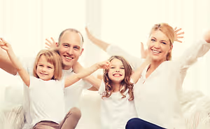 A family of four is sitting on a couch and posing for a photo with their arms raised