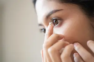 Close up of woman's hand holding contact lens in front of her eye