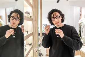 Man wearing glasses adjusting them in front of a mirror