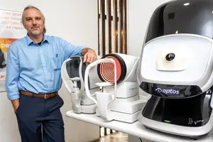 A man is standing next to a table with medical equipment, smiling and posing for a photo.
