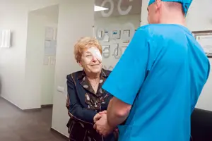 A woman with a bandaged eye talks to a man in blue scrubs in a medical office