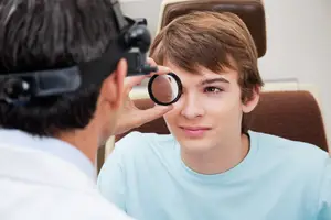 An eye doctor examining a young boy's eyes with a magnifying glass.