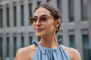 A woman with brown hair wearing sunglasses and a blue sleeveless top standing in front of a building