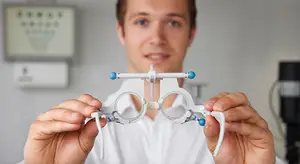 A young man in an optometrist's office is holding a pair of eyeglass frames in his hands.