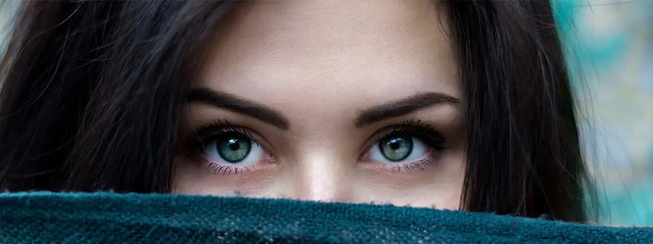 Closeup of a womans face with her eyes peeking out from behind a green cloth