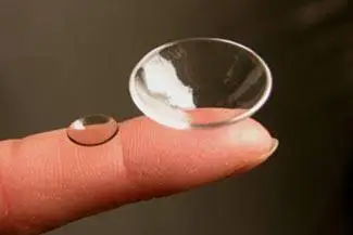 Close up of a finger holding a contact lens with a smaller lens behind it.