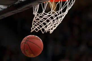 A basketball being shot into the hoop in a sports court.