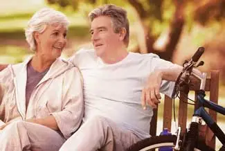 An elderly couple sitting on a bench and smiling with a bicycle in the background
