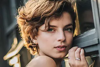 A woman with short curly hair and a serious expression, looking out of a window.