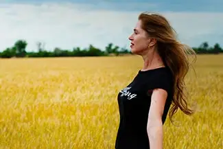 A woman with long red hair wearing a black shirt is standing in the middle of a field.