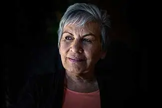 Portrait of an older woman with short gray hair wearing a pink shirt and smiling at the camera