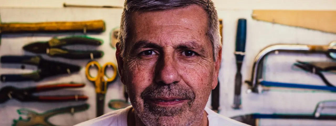 A man in a workshop with tools on the wall behind him