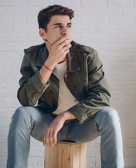 A man in a green jacket and blue jeans sitting on a wooden box and posing for a picture
