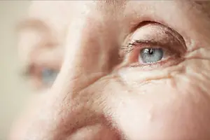 Close-up of an elderly person with a wrinkled face and brown eyes looking at something in front of them.