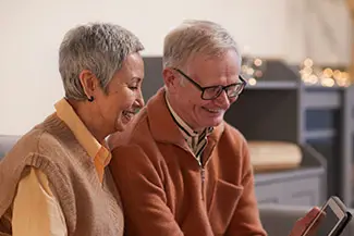 An elderly couple sitting next to each other smiling while looking at their phones
