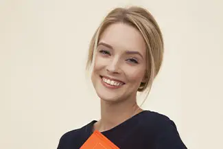 Blonde woman smiling and holding an orange passport cover