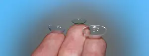 Three transparent contact lenses on a finger against a blue background