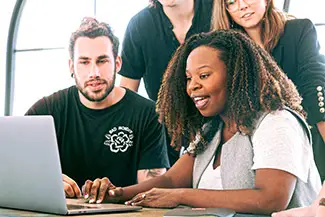 Three people sitting around a table looking at a laptop with one woman smiling at the camera