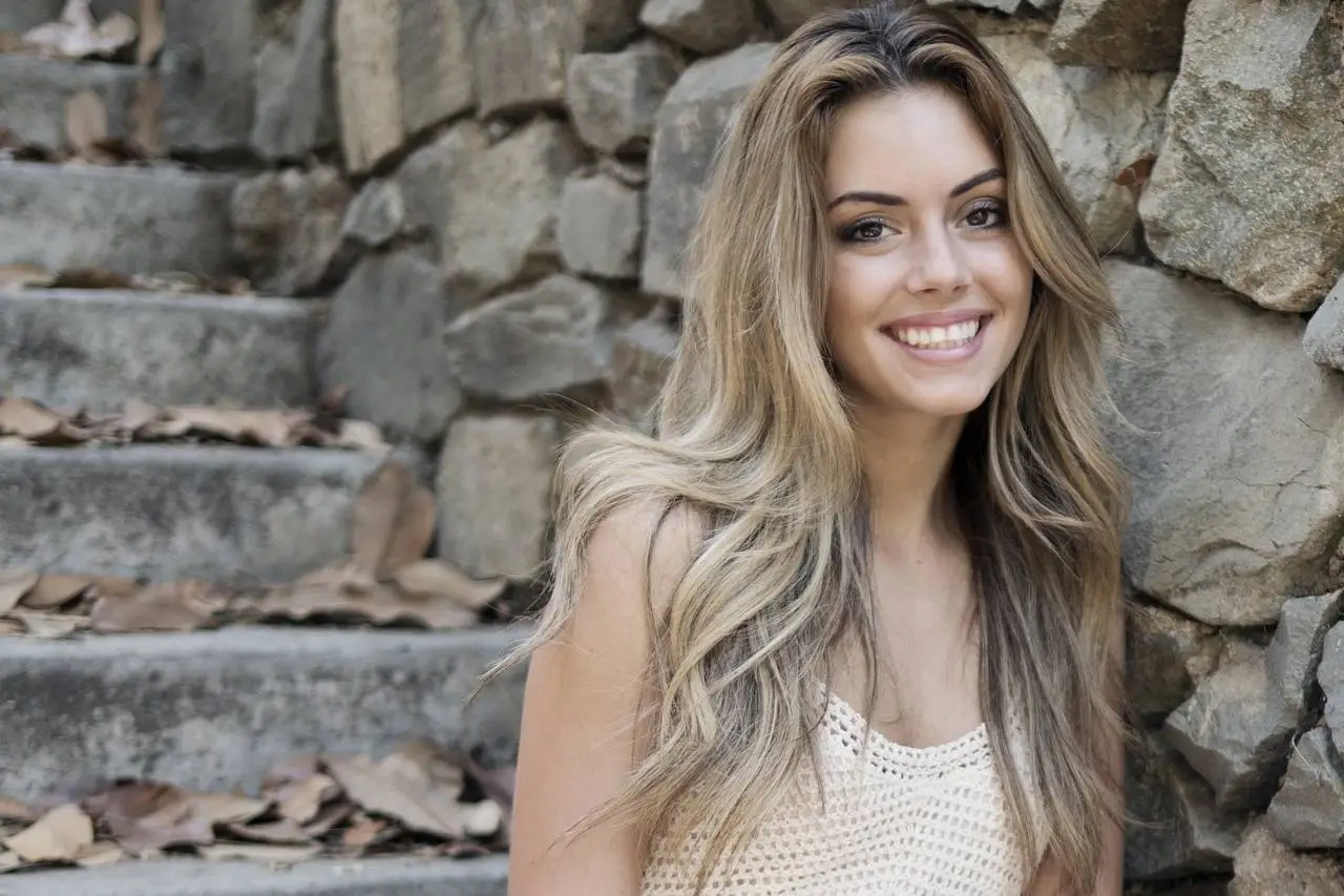 Beautiful woman with blonde hair smiling against a stone wall with stairs in the background