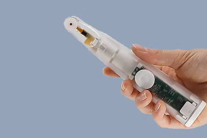 A hand holding a transparent medical device with a camera and a green circuit board.
