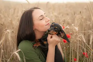 A woman holding and kissing her dog in a wheat field