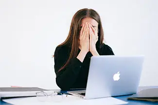 woman sitting at a desk with her hands over her face and looking upset