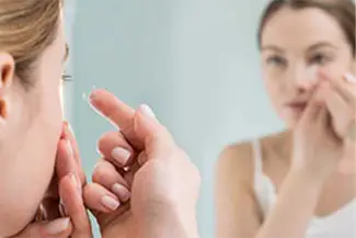 Woman putting in contact lenses in front of a mirror