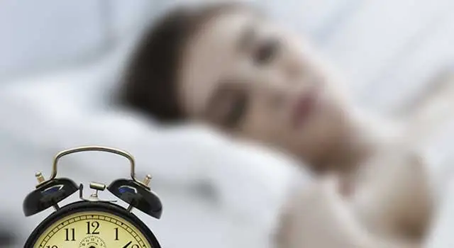 Image of a woman sleeping in bed with an alarm clock beside her