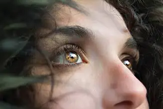 Close-up of a woman's face with curly hair and amber eyes looking up