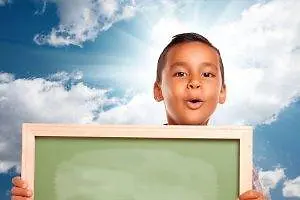 A young boy is holding a blackboard with both hands and posing for the camera