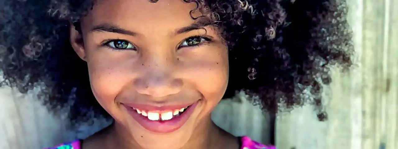 young girl with curly black hair wearing a pink and white top with a smiling face