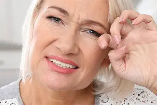Blonde-haired woman touching her eyebrow with a smile