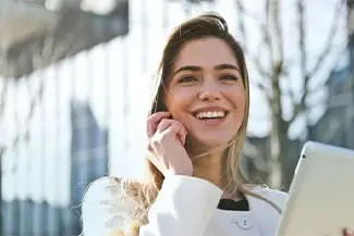A smiling woman holding a tablet in front of a building