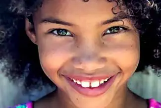 A young girl with curly hair and green eyes smiling