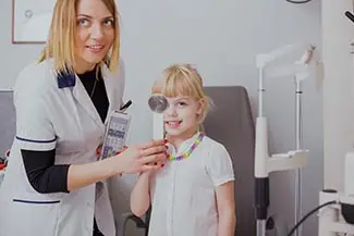 An adult woman is checking the vision of a young girl with an ophthalmoscope in a medical setting.