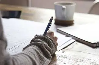 A person sitting at a desk and writing on a piece of paper using a pen