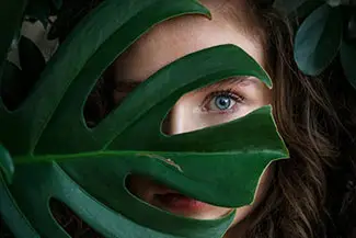 A woman with blue eyes hiding behind a large green leaf.