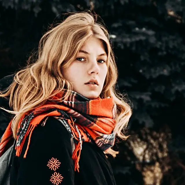 Blonde woman wearing a plaid scarf in front of trees