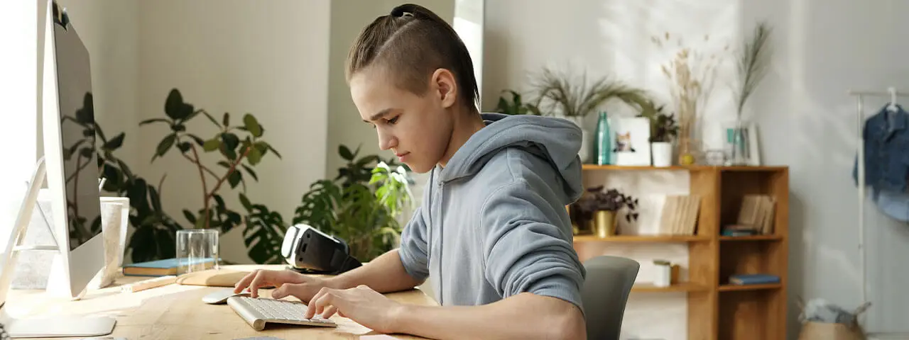 A young boy sits at a desk and types on a computer keyboard