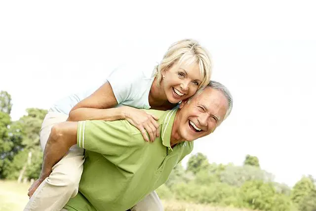 A smiling older man is carrying a smiling older woman on his back