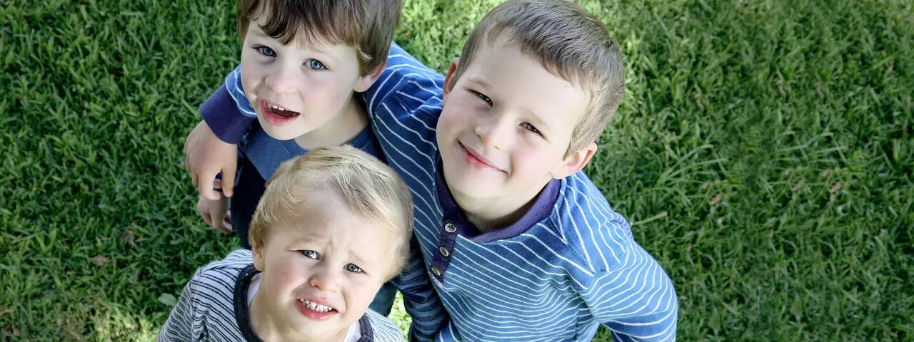 Three boys are smiling on a grassy field.