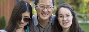 A man and two women, all smiling for a family photo in front of a fence.
