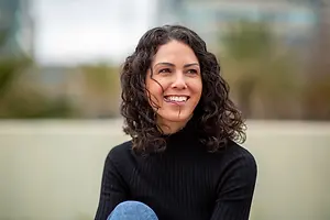 Curly-haired woman sitting outdoors and smiling for a portrait