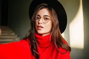 A woman with long brown hair wearing a red turtleneck shirt and a black hat takes a selfie.
