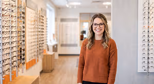 A woman with glasses is standing in a room with many frames hanging on the wall