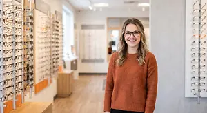 A woman with glasses is standing in a room with many frames hanging on the wall