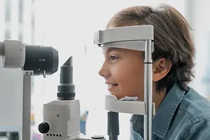 A young boy is smiling and looking into an ophthalmoscope in a medical setting.